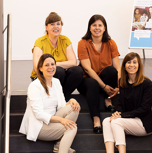 4 Frauen sitzen lächelnd auf einer Treppe